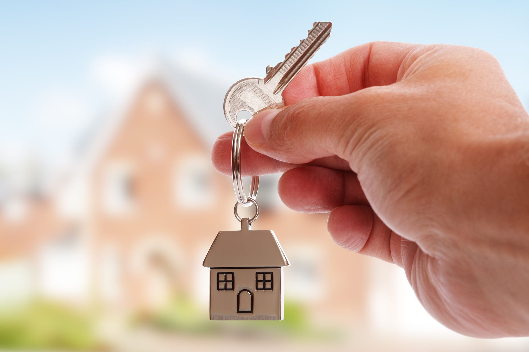 Holding house keys on house shaped keychain in front of a new home